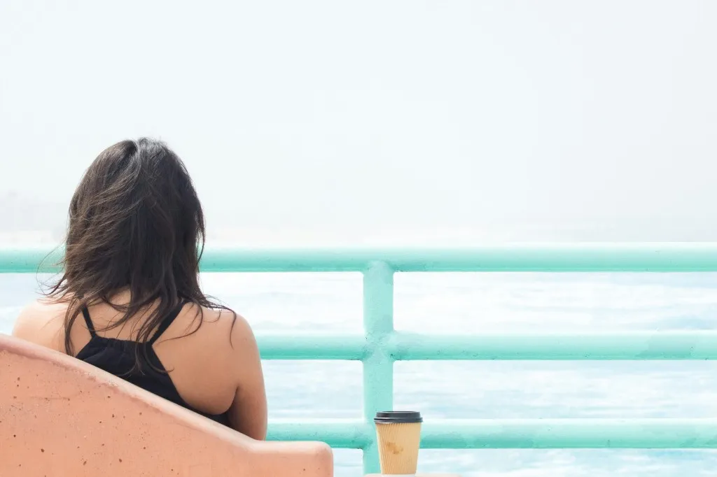 Woman sitting on a seafront bench with a takeaway coffee, looking out over the water