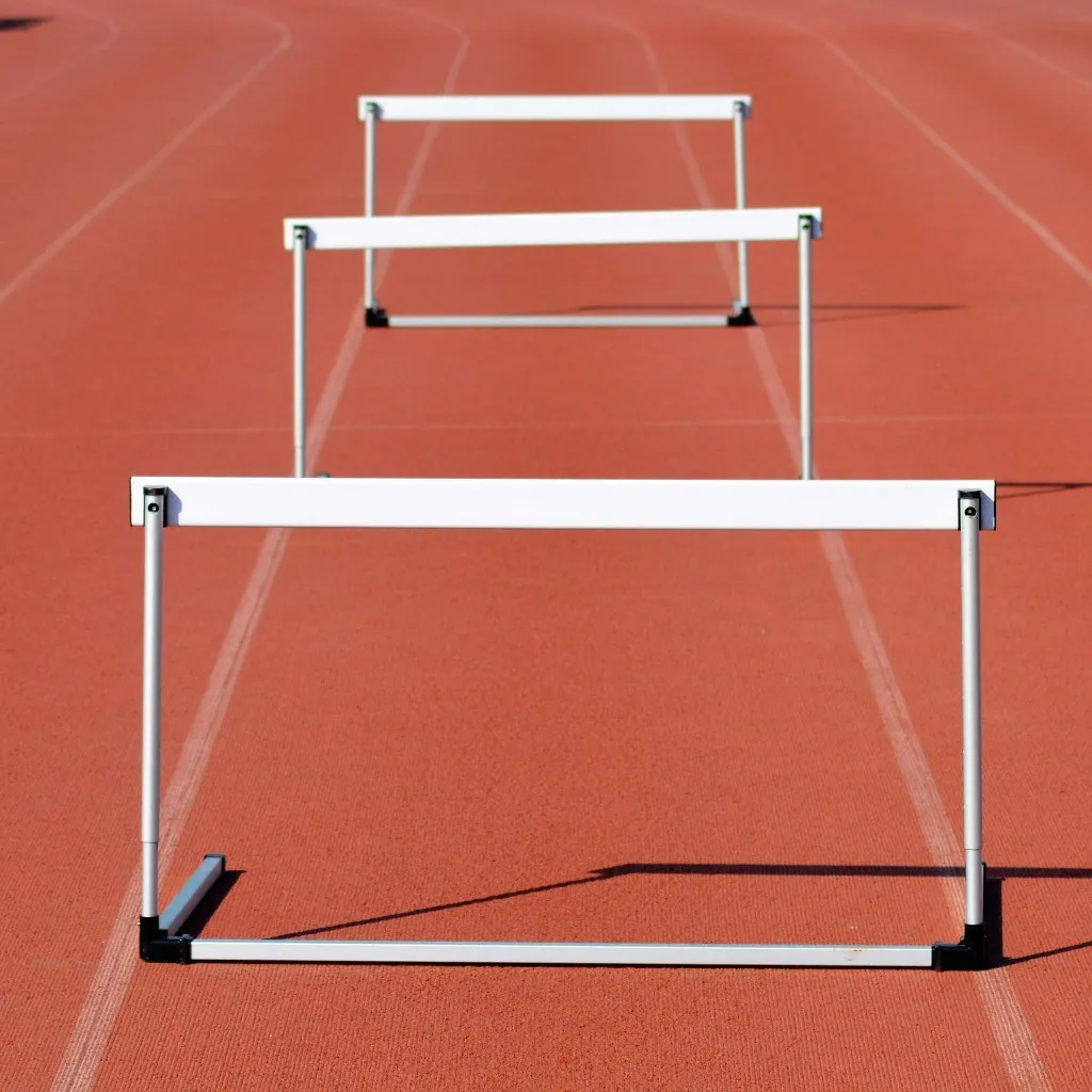 Three hurdles on a red athletics track, representing obstacles to overcome