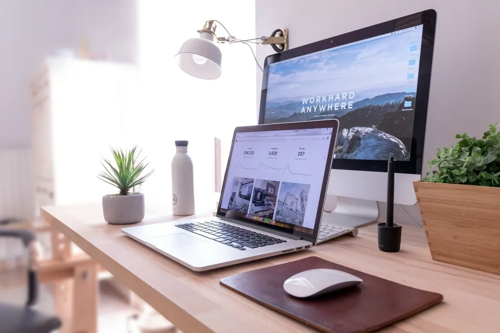 Minimal desk setup with a laptop showing a website portfolio and a monitor displaying a mountain landscape