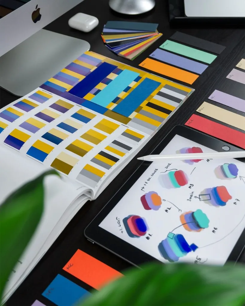 Designer's desk with colour swatches, a tablet showing brand palettes, and design tools