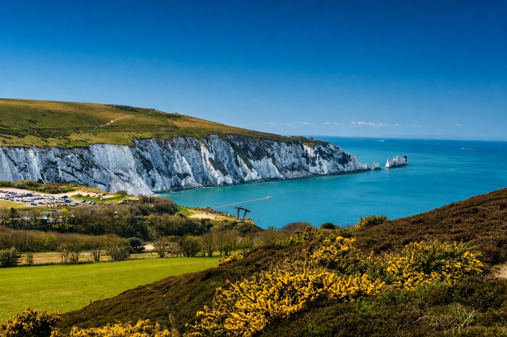 Alum Bay and the Needles on the Isle of Wight in summer, white chalk cliffs, turquoise sea, and gorse on the hillside.